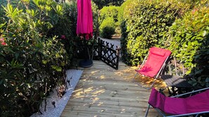 A wooden deck with a red chair and umbrella, surrounded by dense greenery and a black metal fence. - Charming studio with garden in St-Raphaël (Saint-Raphaël)