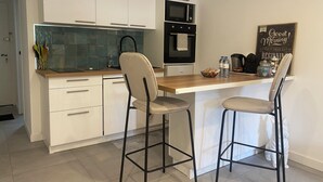 A modern kitchen with white cabinets, a wooden countertop, two bar stools, a microwave, and a kettle. - Charming studio with garden in St-Raphaël (Saint-Raphaël)