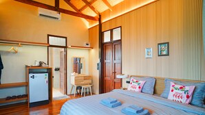 A bedroom with a bed, a desk, a chair, a small refrigerator, and a wardrobe.