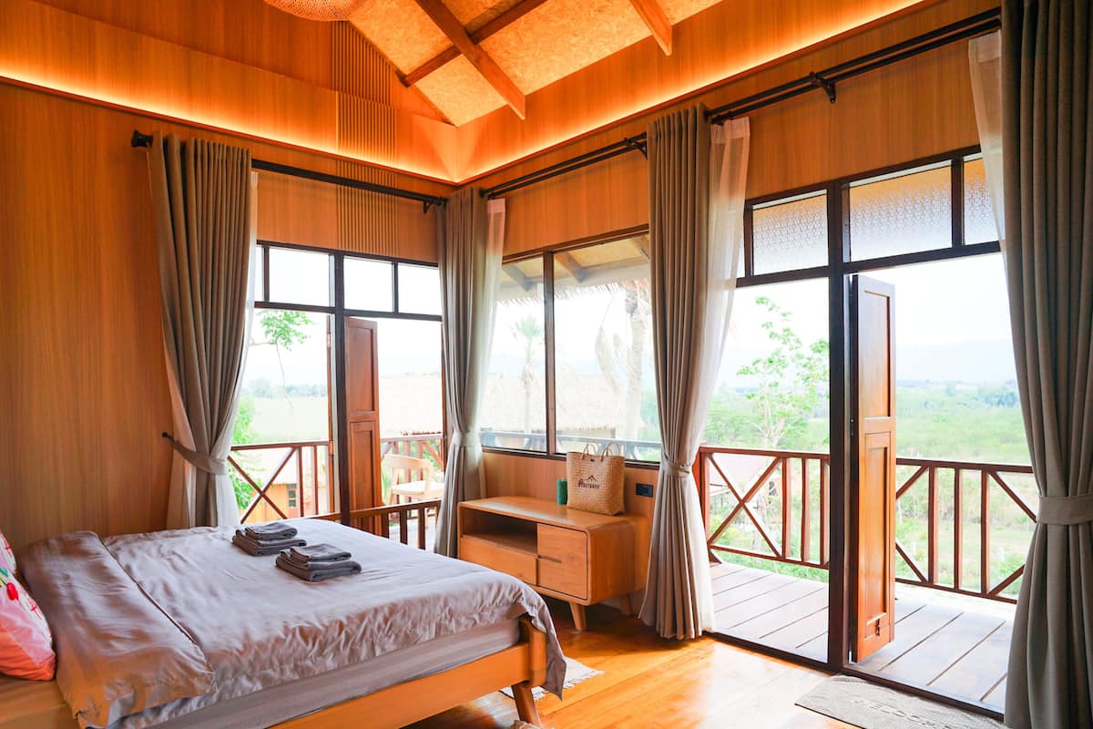 A bedroom with a bed, a desk, and a view of the outdoors.