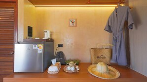 A kitchenette with a refrigerator, a hair dryer, a tea set, a woven bag, and a hat on a wooden counter.