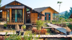 A bungalow-style hotel with thatched roofs, wooden balconies, and a garden pathway.