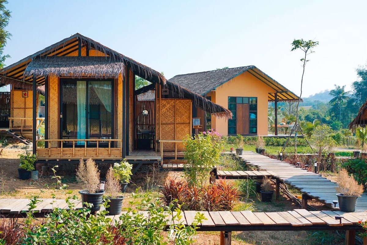 A bungalow-style hotel with thatched roofs, wooden balconies, and a garden pathway.