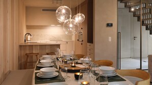 A modern dining area with a long table set for a meal, a kitchen in the background, and a staircase leading to another level. - Woodz Lodges - Groepslodge | 10p (Heusden-Zolder)