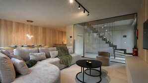 A modern living room with a sectional sofa, a round coffee table, and a staircase leading to an upper level. - Woodz Lodges - Groepslodge | 10p (Heusden-Zolder)