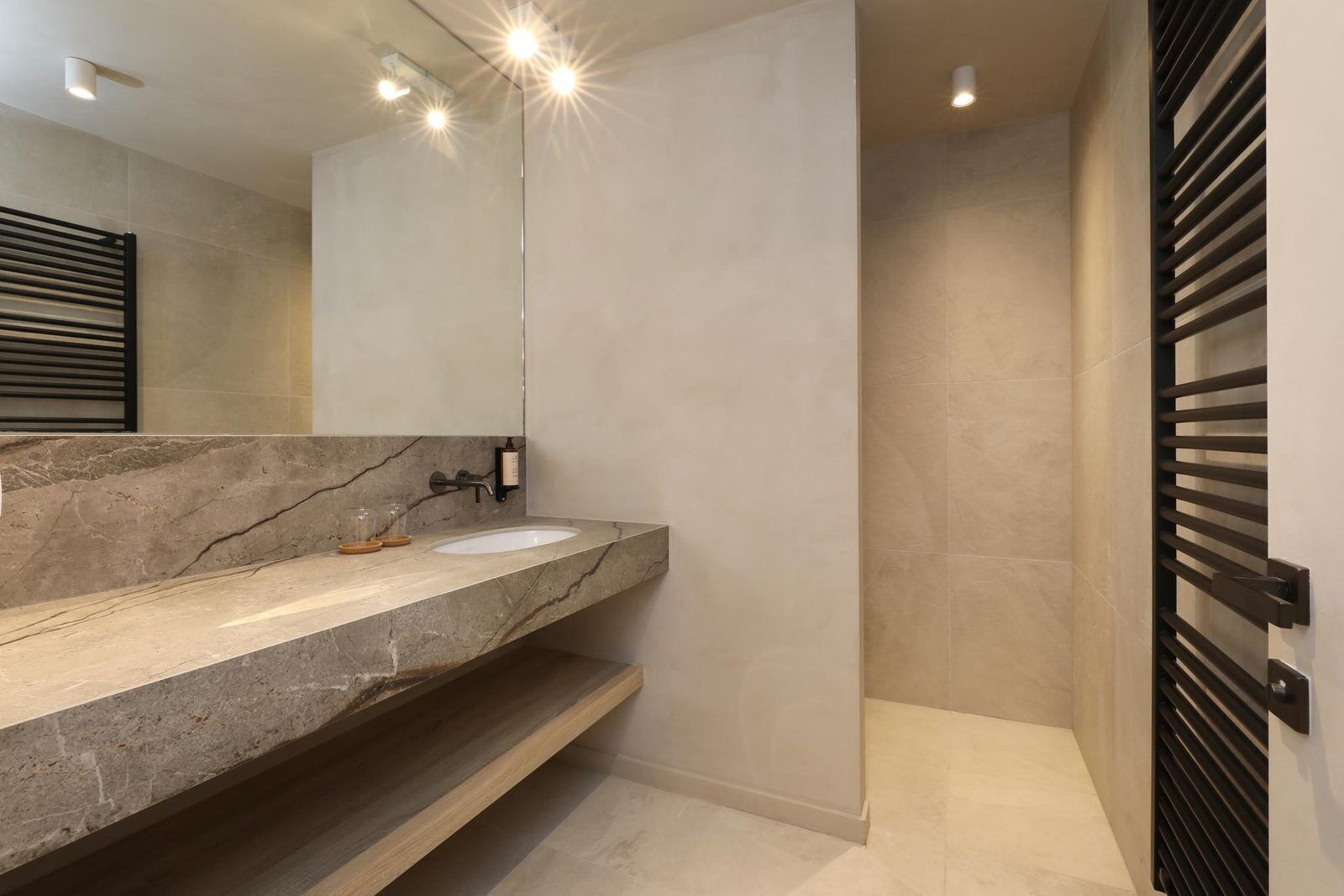 Ein modernes Badezimmer mit Marmorplatte, zwei Waschbecken, einem großen Spiegel und einer Duschkabine.