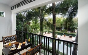 Un balcon avec une table à manger dressée pour le petit-déjeuner, offrant une vue sur une piscine et une végétation luxuriante.
