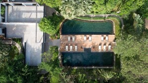 Vue aérienne d’un complexe hôtelier doté d’une piscine, de chaises longues et d’un bâtiment moderne, le tout entouré d’une végétation luxuriante.
