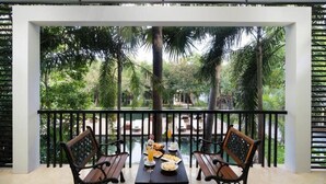 Un balcon avec une table dressée pour deux personnes, entouré d’une végétation luxuriante et de palmiers.