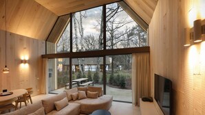 Un interior moderno con un ventanal grande, paredes de madera, un sofá, una mesa de comedor y un televisor.