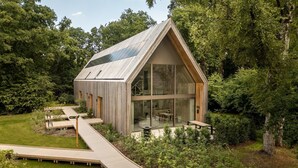Una casa moderna con techo inclinado, amplios ventanales y una terraza de madera.