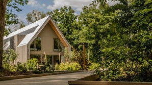 A modern house with a sloped roof, surrounded by lush greenery and a paved pathway.