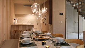 A modern dining area with a wooden table set for a meal, a kitchen in the background, and a staircase leading to another level.