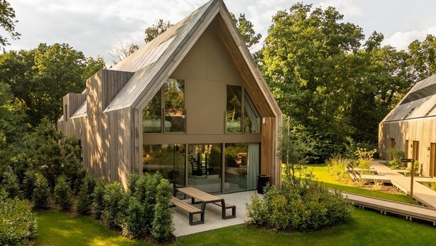 A modern house with a sloped roof, large windows, and a patio area.