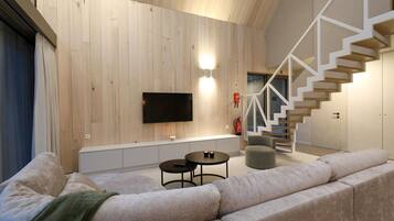 A modern living room with a wooden wall, a flat-screen TV, a staircase, and a sofa.