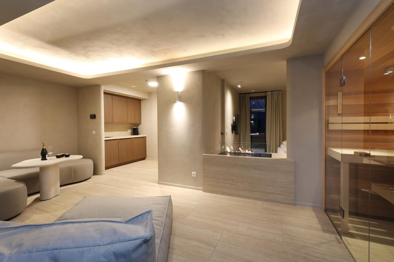 Een moderne woonkamer met een bank, een glazen salontafel, een keukenhoek en een open haard.