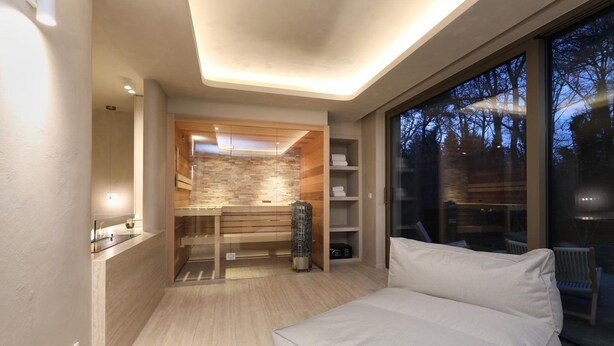 Una habitación moderna con un banco empotrado, cabina de ducha de vidrio y un ventanal con vistas a árboles.
