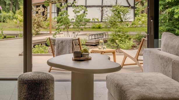 Interior moderno com uma mesa redonda, duas poltronas e vista para uma casa tradicional através de grandes janelas.
