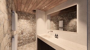 Uma casa de banho com parede de pedra, teto de madeira, lavatório com duas garrafas e espelho.