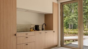 Uma cozinha moderna com fogão embutido, cafeteira e vista para um jardim através de uma porta de correr.
