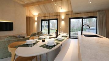 A modern dining area with a long table set for four, a sofa, and a TV mounted on the wall.