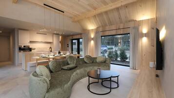 A modern interior with a curved sofa, dining table, kitchen area, and large windows.