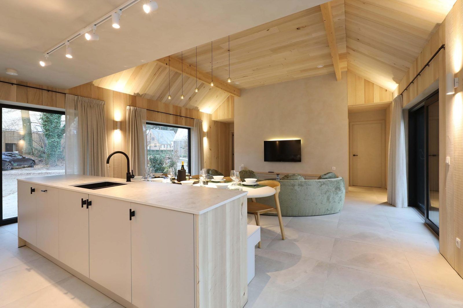 A modern kitchen with a large island, a dining area with a sofa, and a TV mounted on the wall.