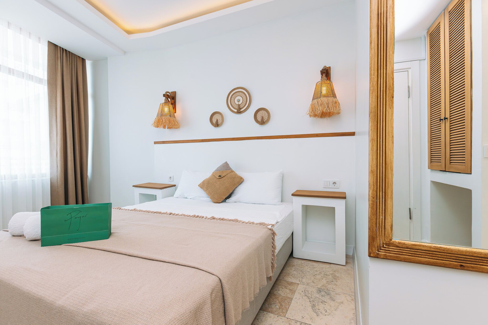 A hotel room with a bed, bedside tables, a mirror, and wall decor.