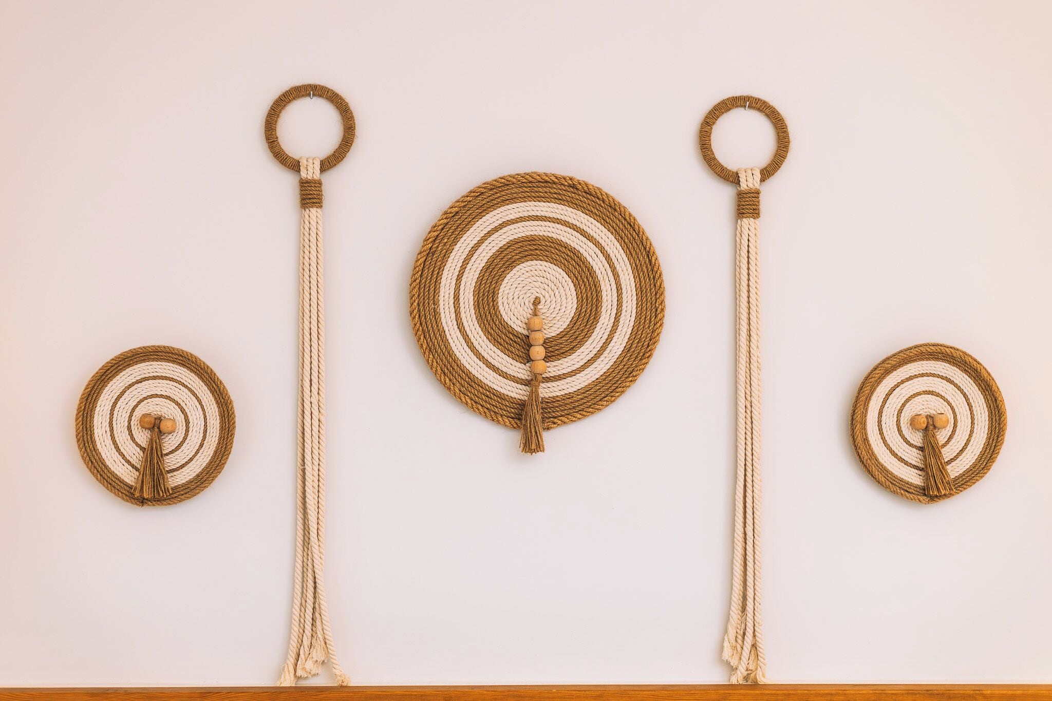 Three macramé wall hangings with tassels and circular rings, mounted on a plain wall.