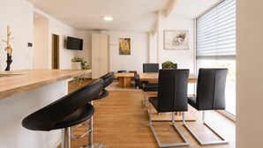 Una cocina moderna con encimera de madera, taburetes negros tipo bar, una mesa de comedor con sillas, un televisor montado en la pared y obras de arte en las paredes.