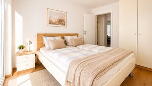 Un dormitorio con cama, mesita de noche, lámpara y una puerta que da a otra habitación.