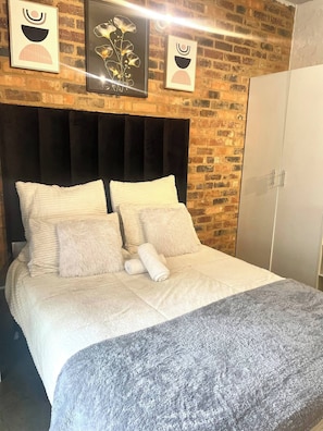 Ein Bett mit schwarzem Kopfteil, weißer Bettwäsche und einer grauen Tagesdecke.