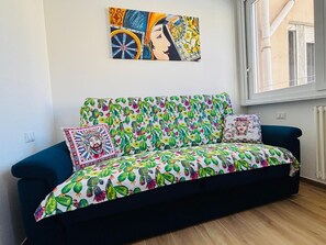 A room with a dark blue sofa, colorful cushions, a wall painting, and a window. - Da Rosalia Apartment: all the comforts in the heart of Palermo's historic center (Palermo)