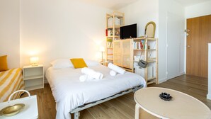 A hotel room with a bed, bedside tables, a television, a wardrobe, and a round table. - Les Embruns – Walk to the Beach, Balcony Included (Fouesnant)