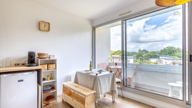A compact kitchen with a refrigerator, wooden bench, and a dining table with chairs. - Les Embruns – Walk to the Beach, Balcony Included (Fouesnant)