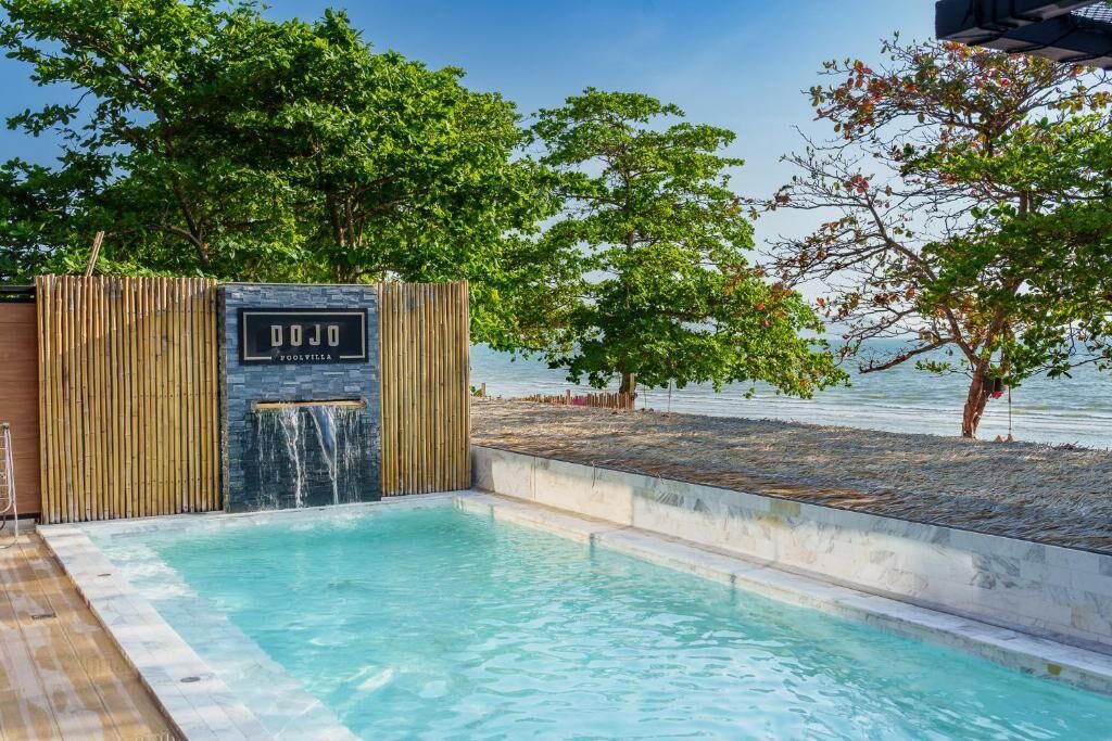 Ein Poolbereich mit Holzzaun, einem Schild mit der Aufschrift 'DOJO' und Blick aufs Meer.