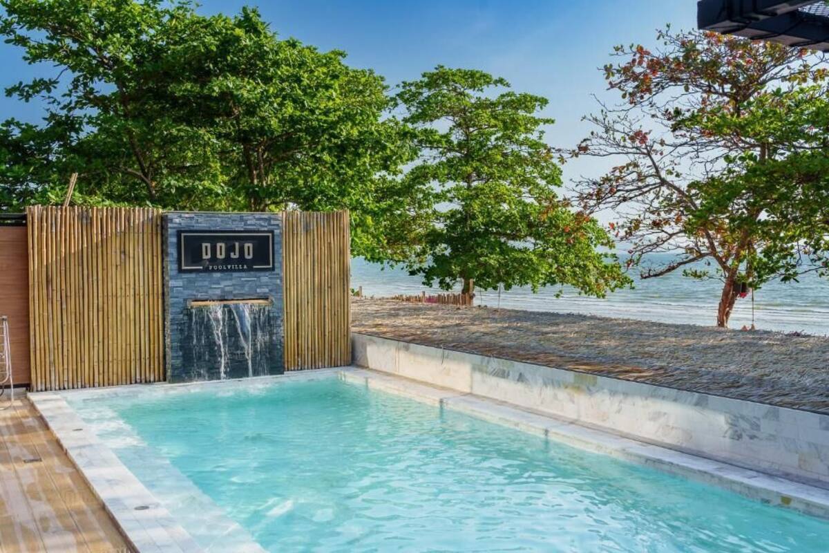 A pool area with a wooden fence, a sign reading 'DOJO,' and a view of the sea.