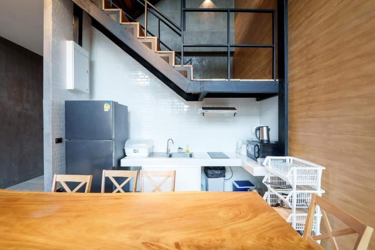 A compact kitchen with a wooden dining table, white cabinets, and a staircase leading to an upper level.