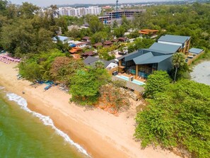 Ein Luftbild eines Küstenresorts mit Strandvillen, einem Swimmingpool und einem Strand mit Sonnenschirmen.
