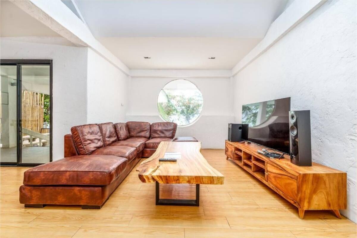A modern living room with a leather sectional sofa, a wooden coffee table, a TV on a wooden stand, and a large circular window.