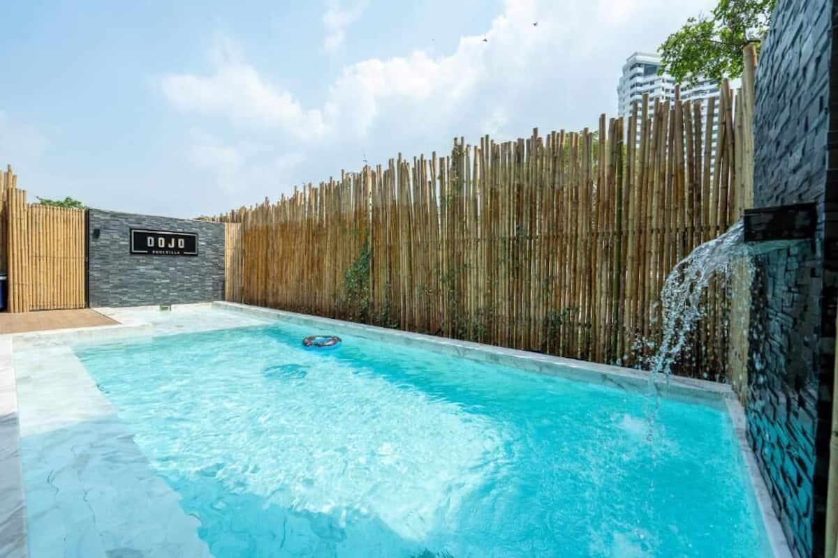 A swimming pool with a wooden fence, a sign reading 'DOJO', and a waterfall feature.