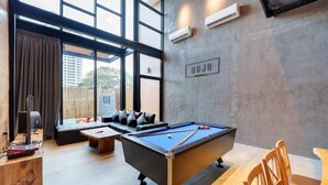 A pool table in a modern room with large windows, a sofa, and a wooden table. - Dojo poolvilla beach resort (Sattahip)