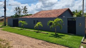 A residential building with a red-tiled roof, a gated entrance, and a well-maintained lawn with palm trees. - Daily or Seasonal Rental in Salinópolis (Salinópolis)