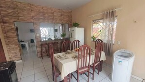 A dining area with a table set for four, a kitchen in the background, and a washing machine near the window. - Daily or Seasonal Rental in Salinópolis (Salinópolis)