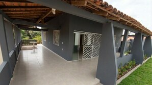 A covered outdoor area with a tiled floor, a wooden ceiling, and a grey wall with a metal gate. - Daily or Seasonal Rental in Salinópolis (Salinópolis)
