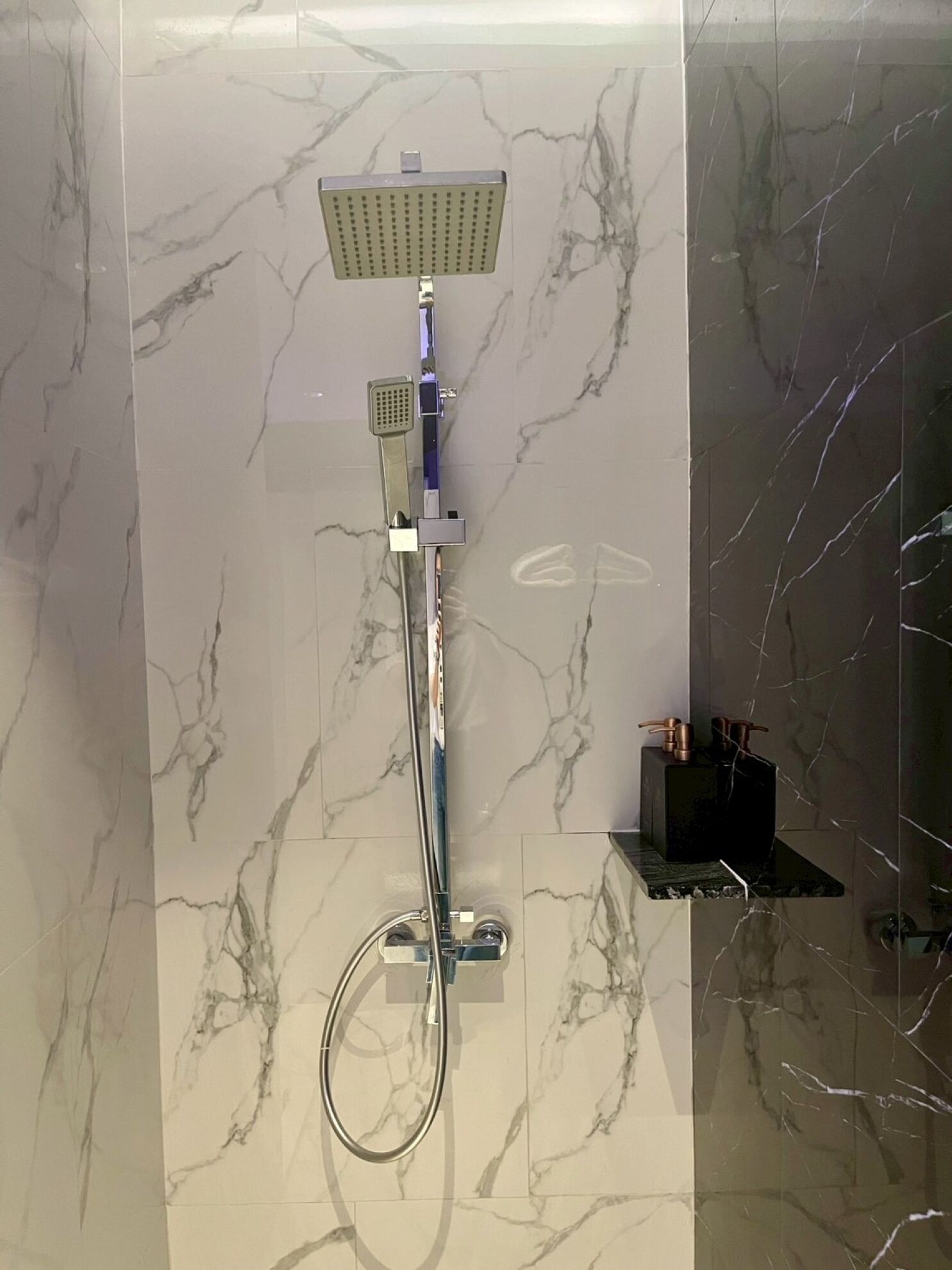 A modern bathroom with a shower, a handheld showerhead, and a handheld faucet.