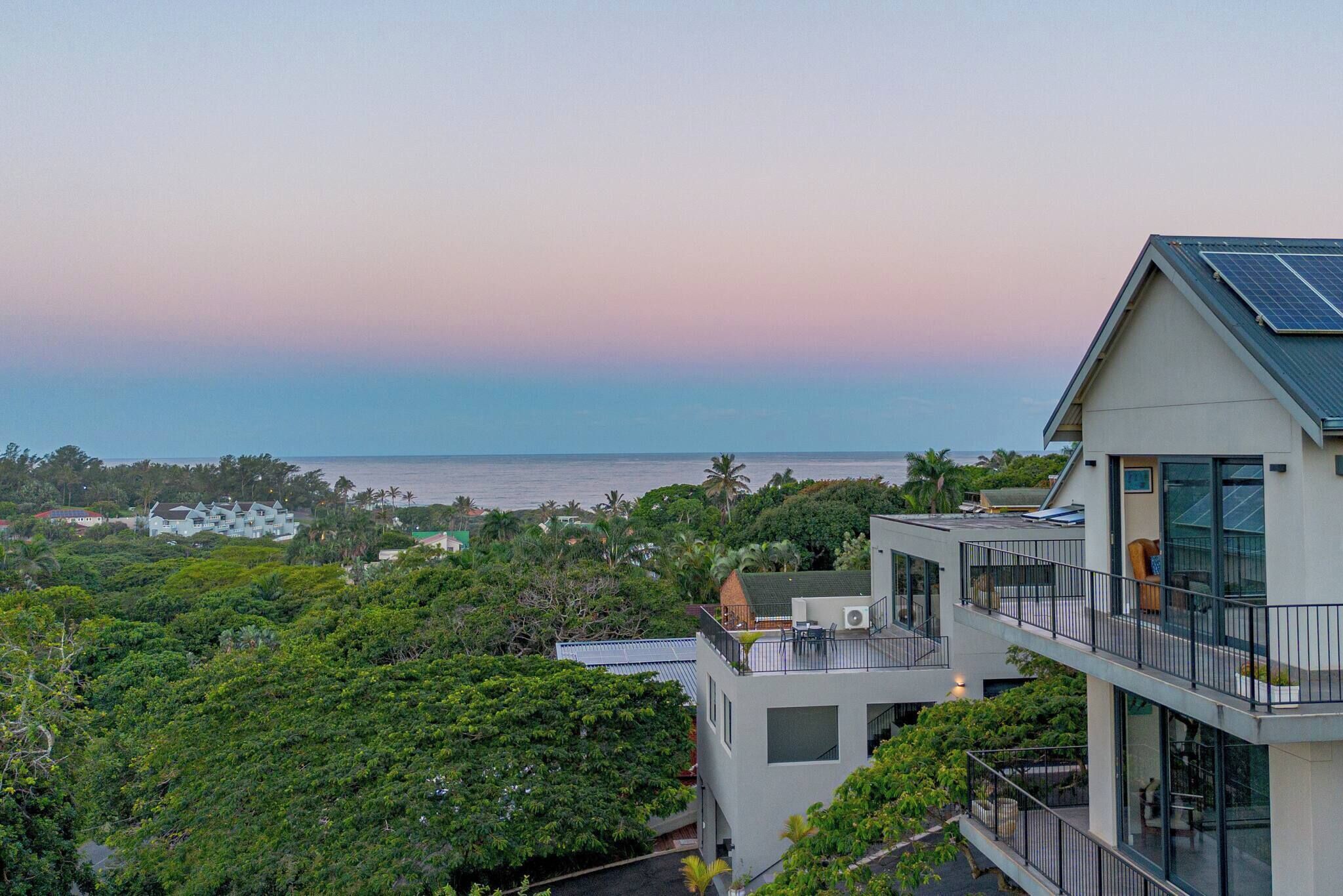 A modern multi-story building with a rooftop terrace, large windows, and a view of the sea.