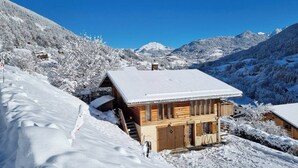 Una baita di legno con un tetto imbiancato dalla neve, circondata da montagne e alberi innevati.