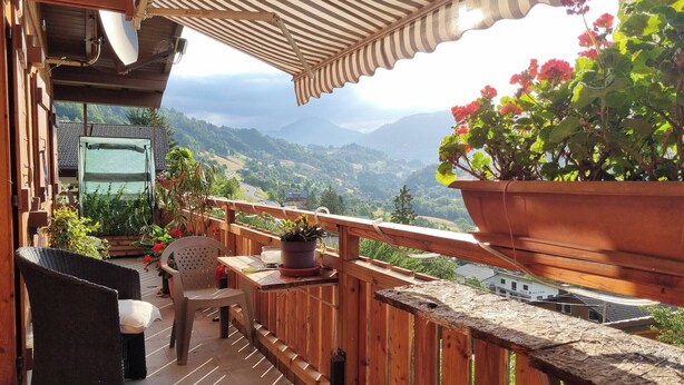 Un balcone in legno con vista sulle montagne, un vaso con una pianta e mobili da esterno.
