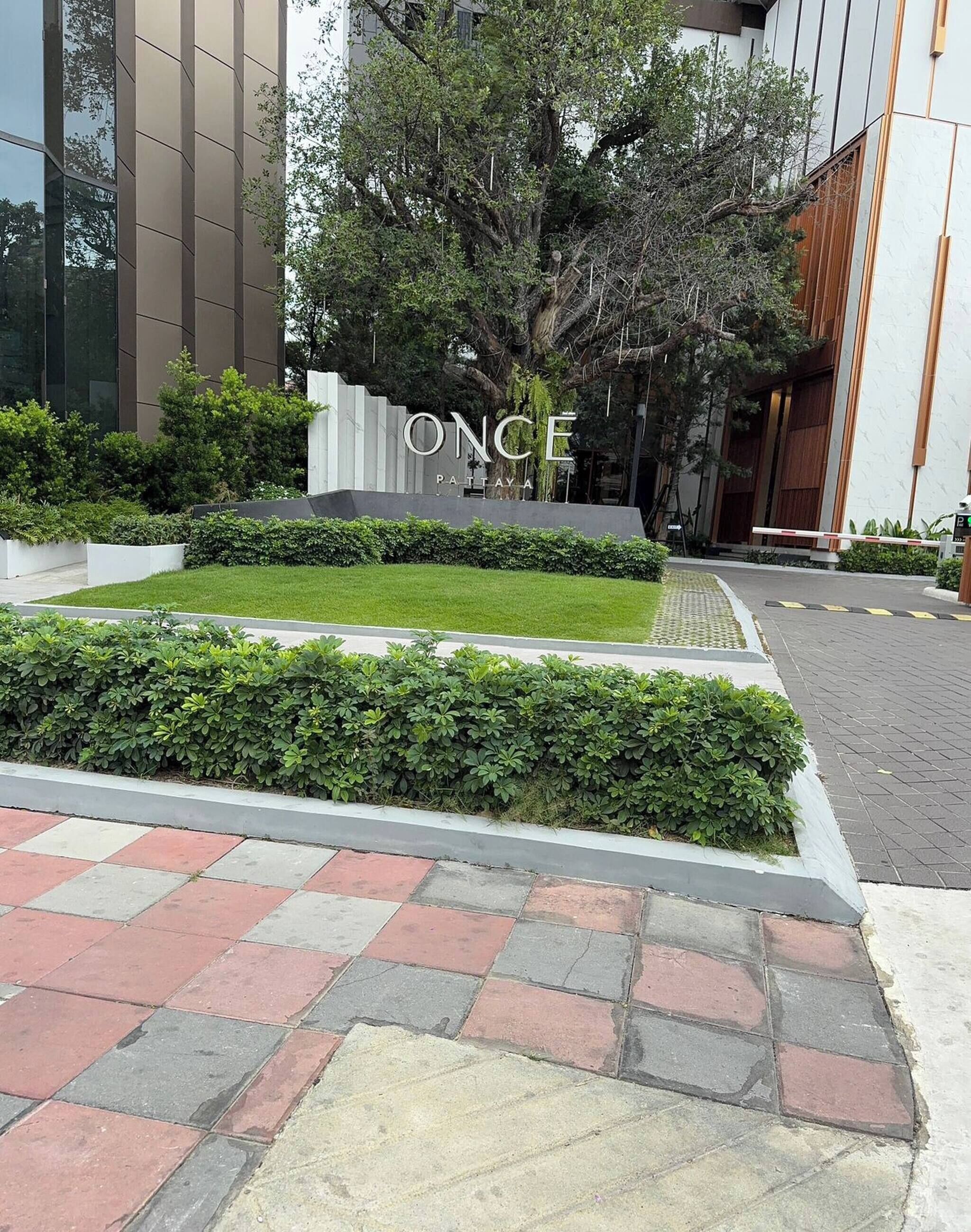 Un edificio moderno con un letrero que dice 'ONCE PATTAYA'. Cuenta con un césped bien cuidado, setos y un camino pavimentado.